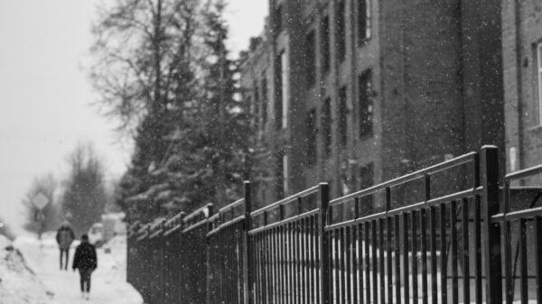 People walking on a snowy sidewalk by a fence