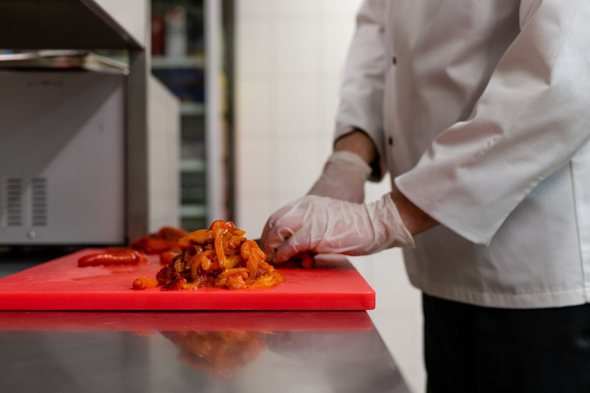 A cook slicing peppers on a red cutting board