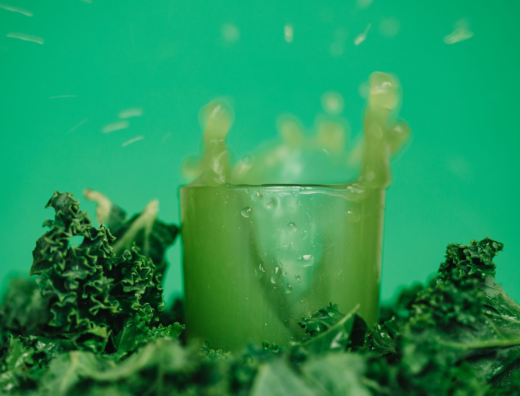 A glass of green juice beside leafy greens