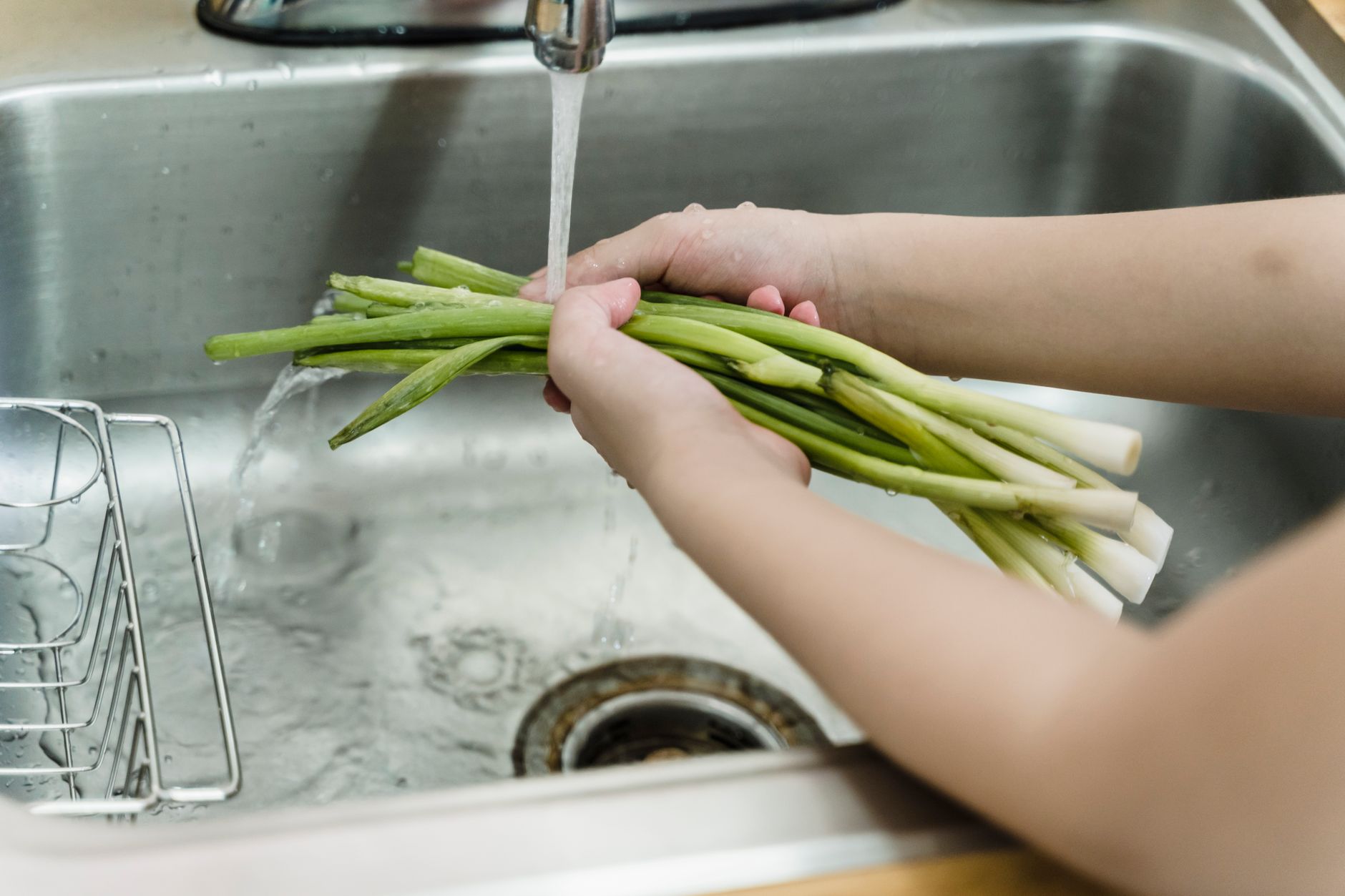 Green onions being rinsed under a faucet