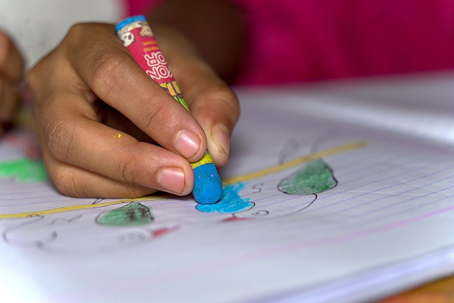 Hands drawing with crayons on paper at a table