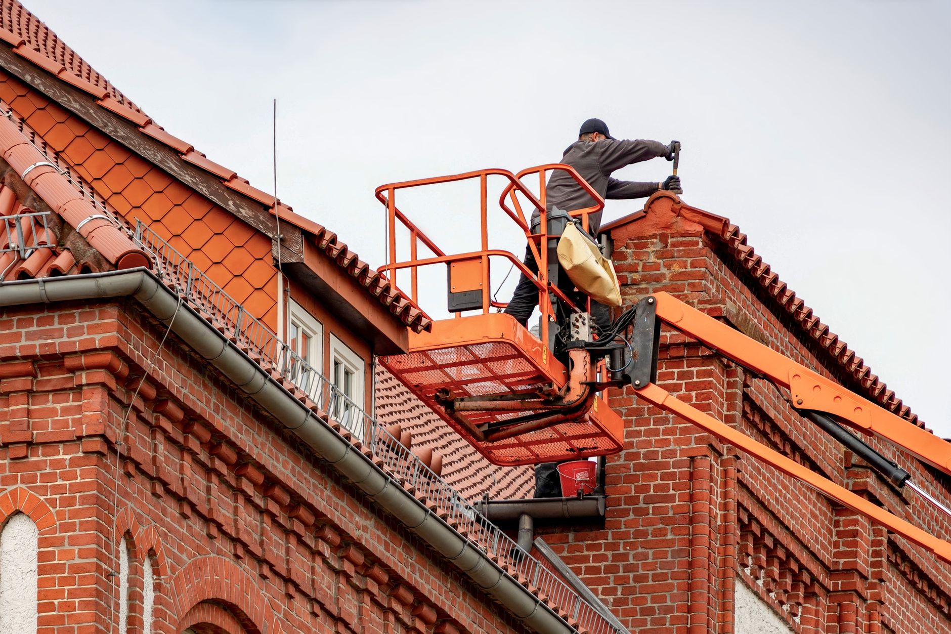 A worker on a lift beside a tiled roof