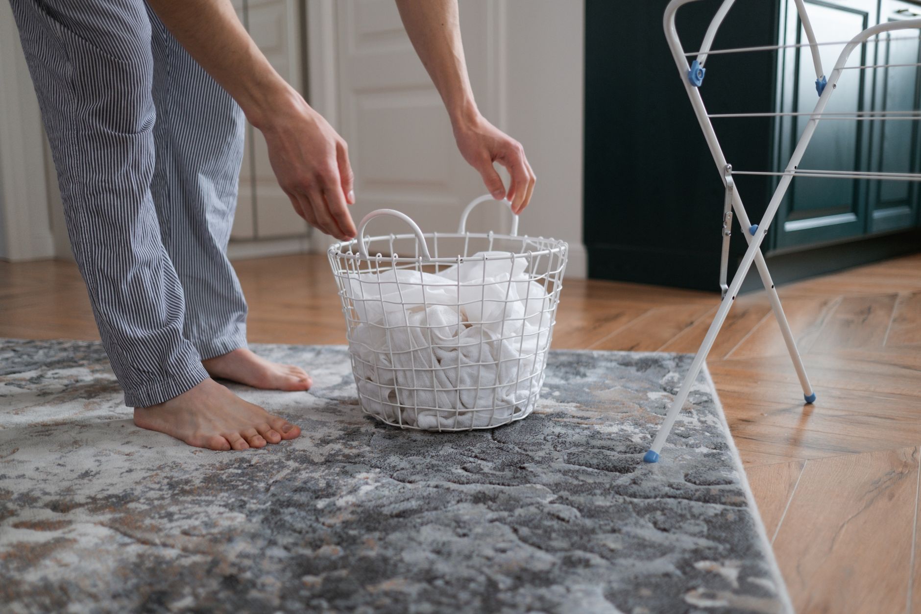 A person picking up a laundry basket by a drying rack