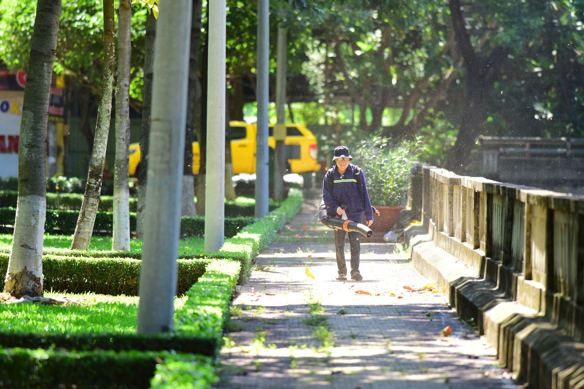 A worker clearing leaves from a path with a blower