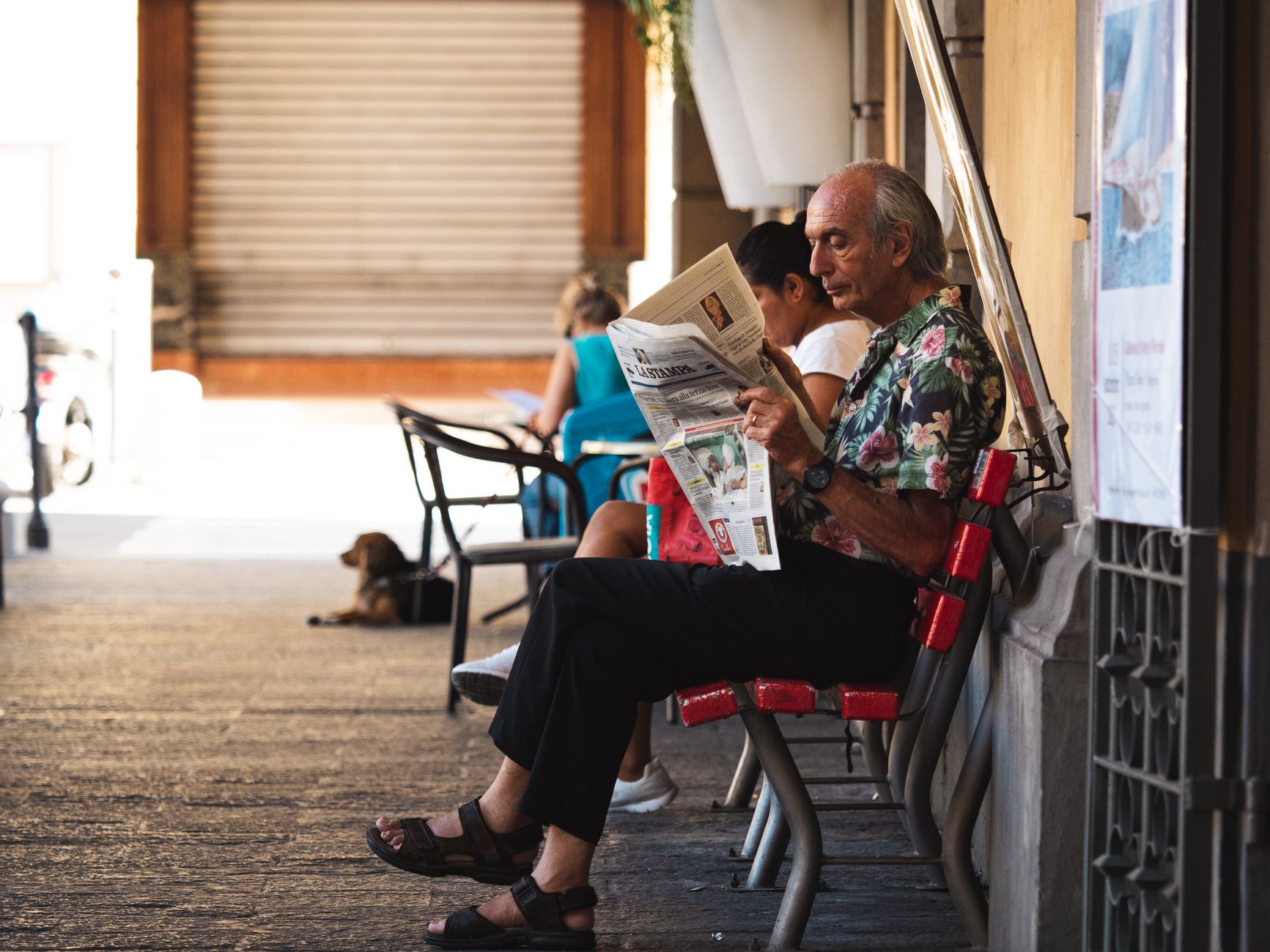 An older man reading a newspaper on a bench