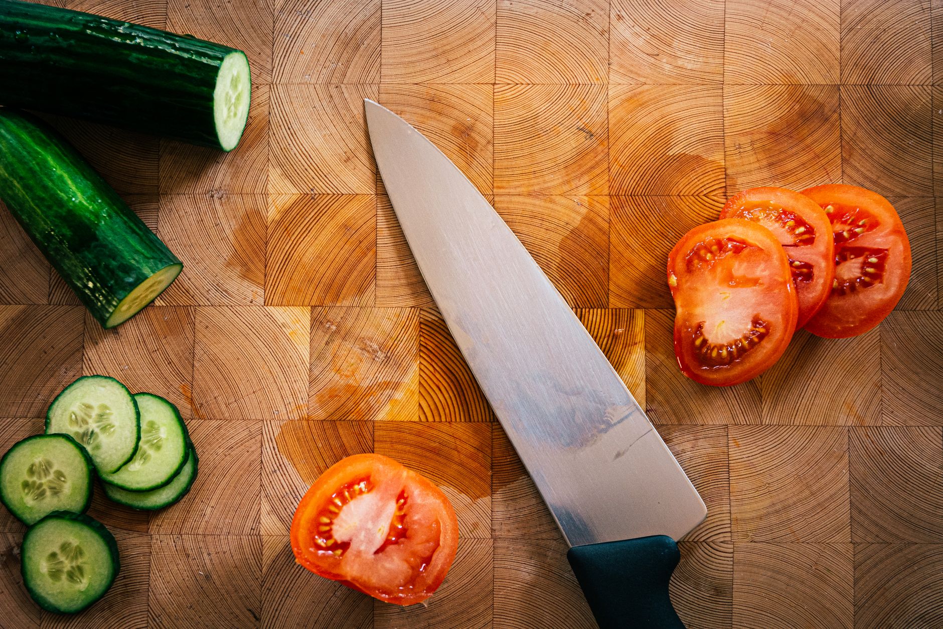 Sliced cucumber and tomato beside a chef knife