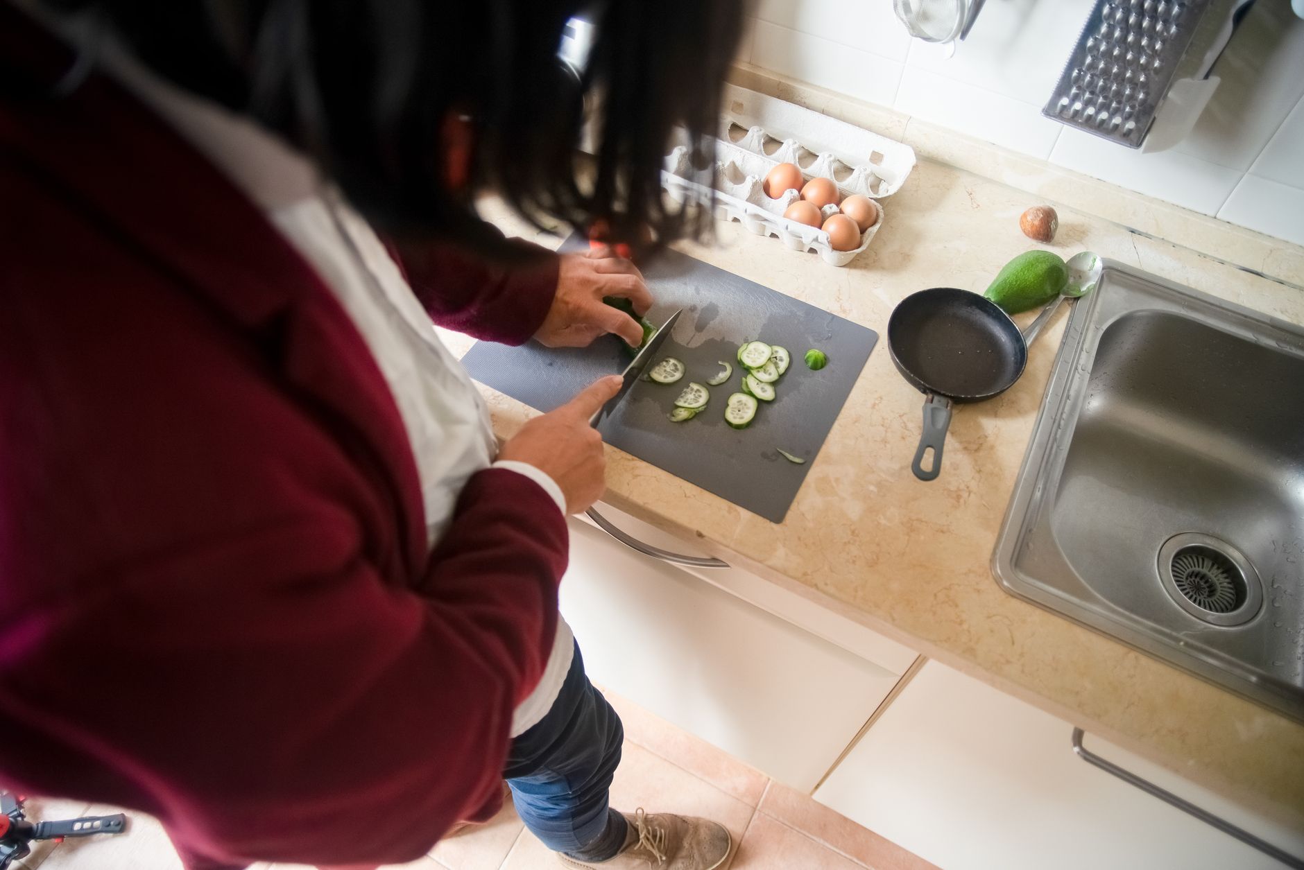 A person slicing cucumber on a kitchen counter