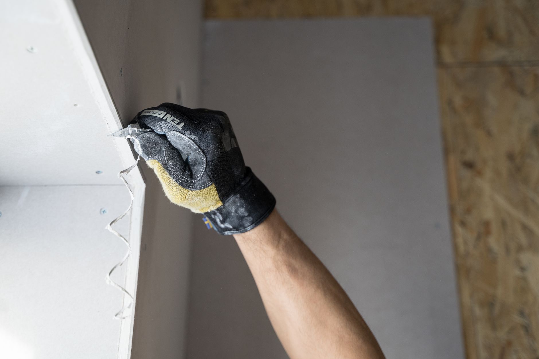 A gloved hand holding a sheet of drywall