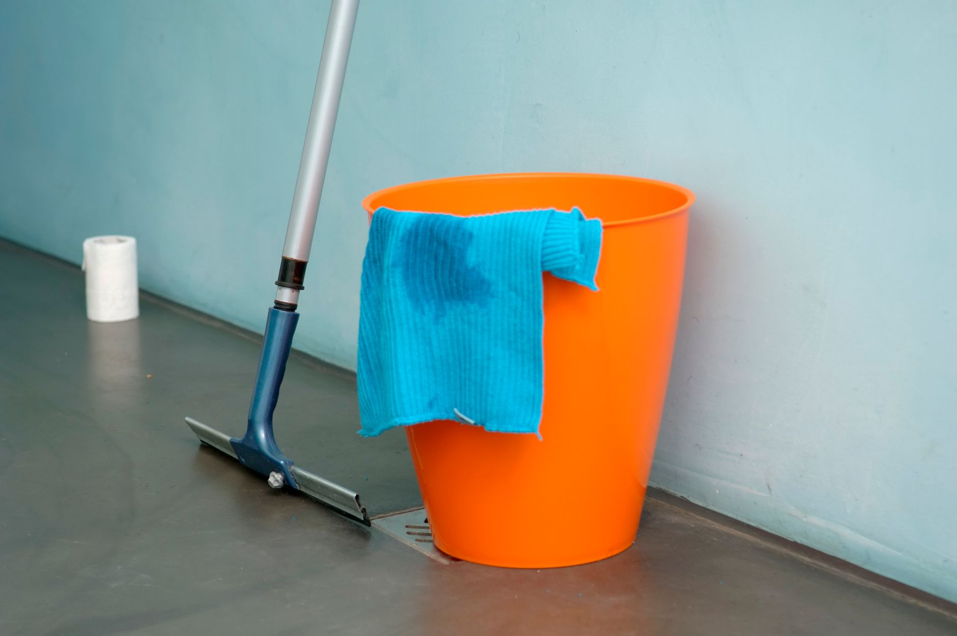 A floor mop leaning on an orange bucket