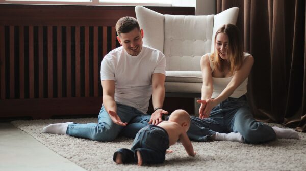 Parents on a rug watching their baby crawl