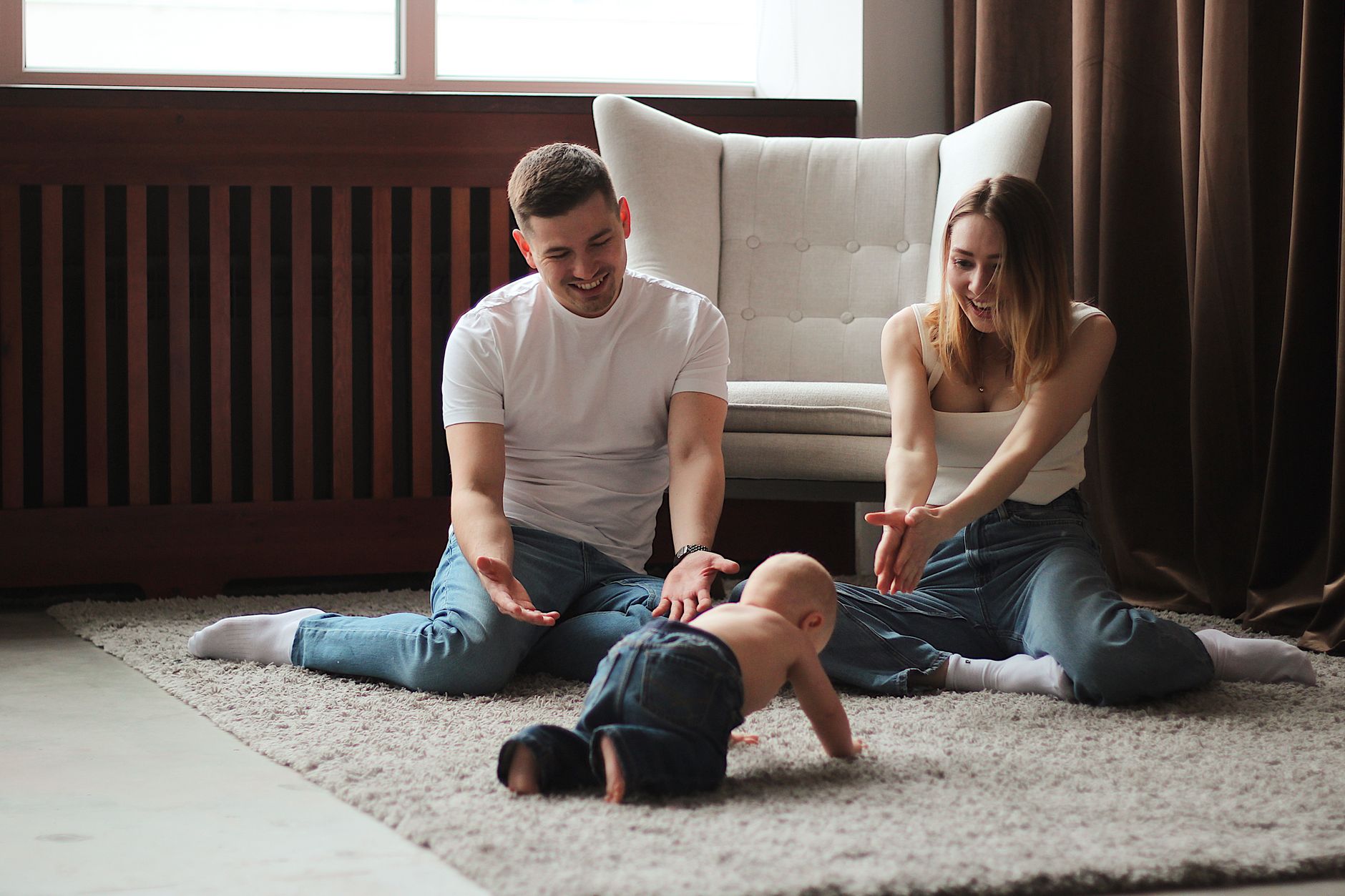 Parents on a rug watching their baby crawl