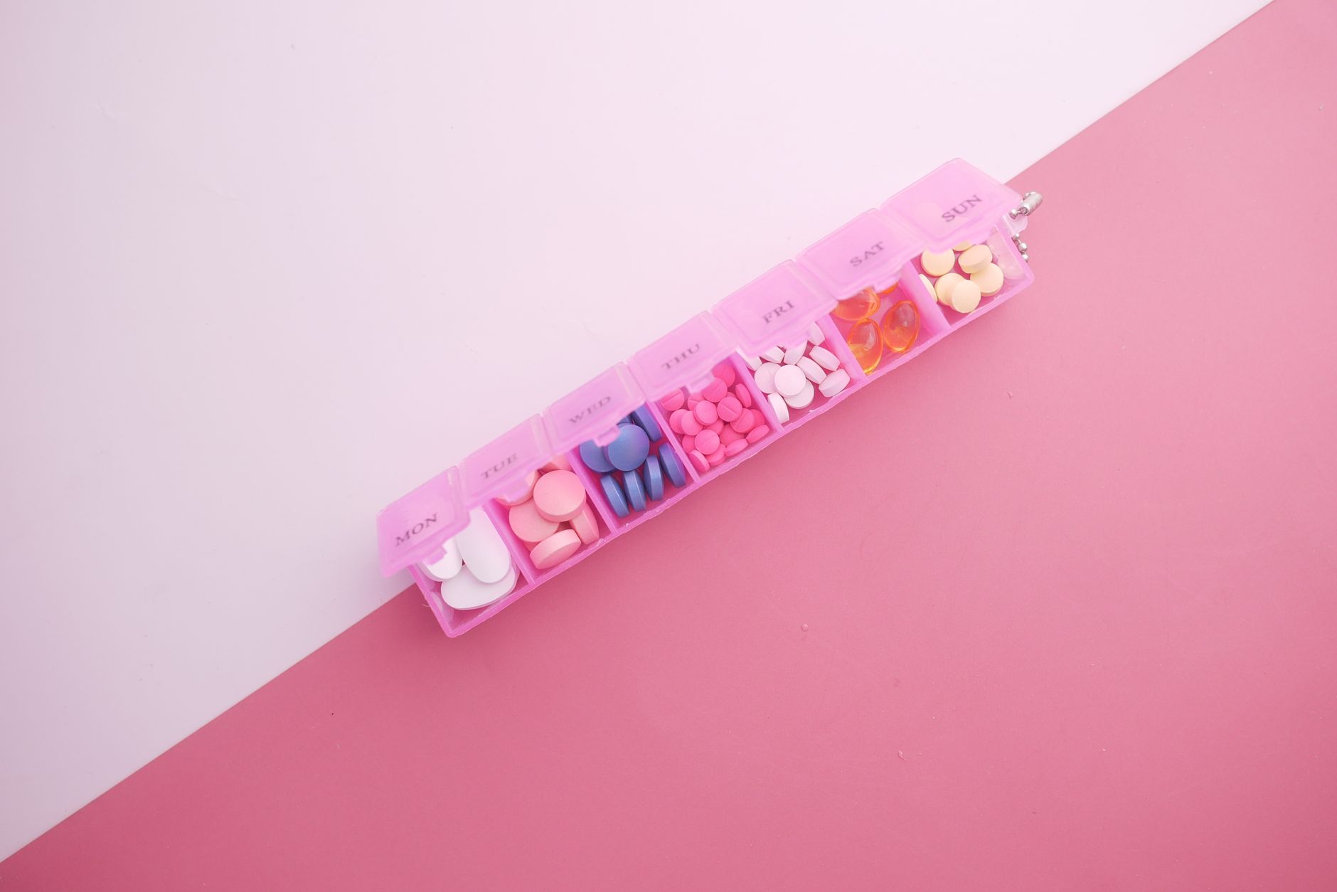 A pink weekly pill organizer filled with tablets