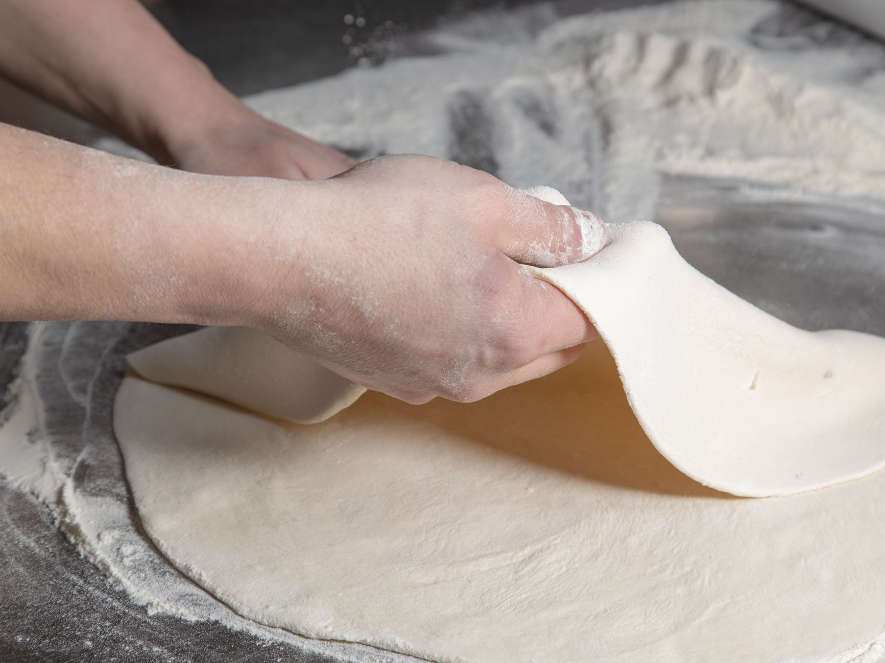Pizza dough being stretched on a floured counter