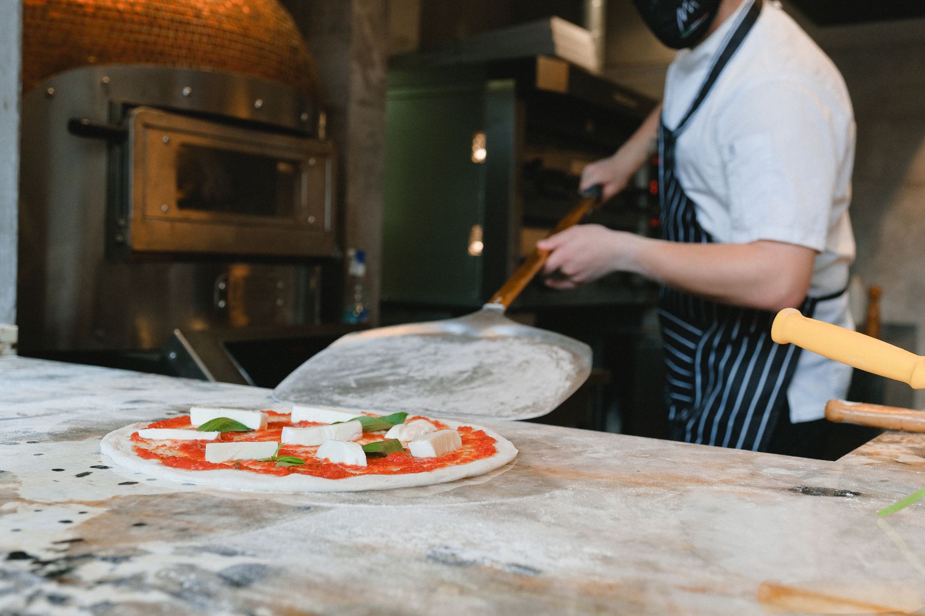A cook sliding a peel under a pizza