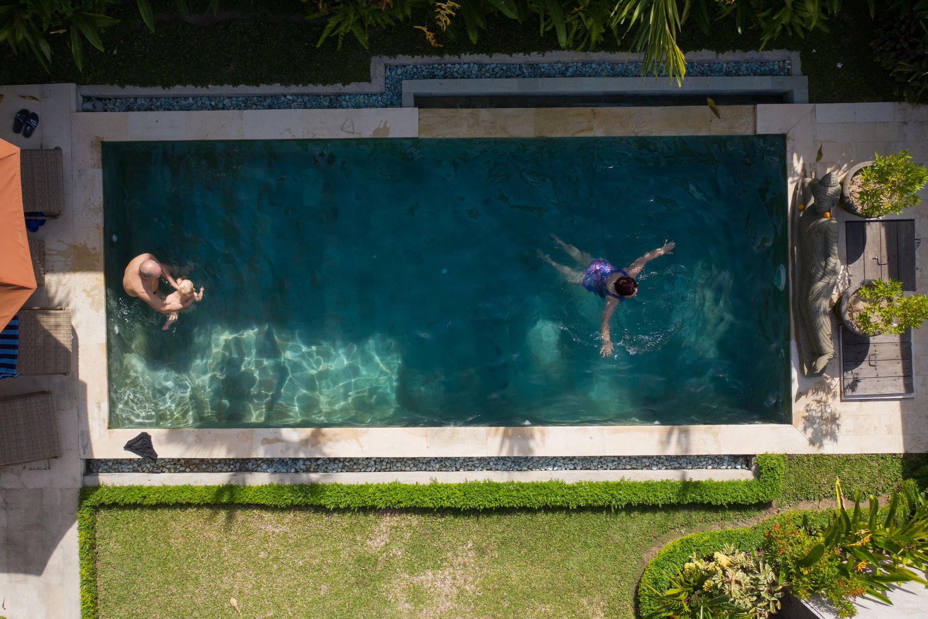 Two people swimming in a backyard pool seen from above