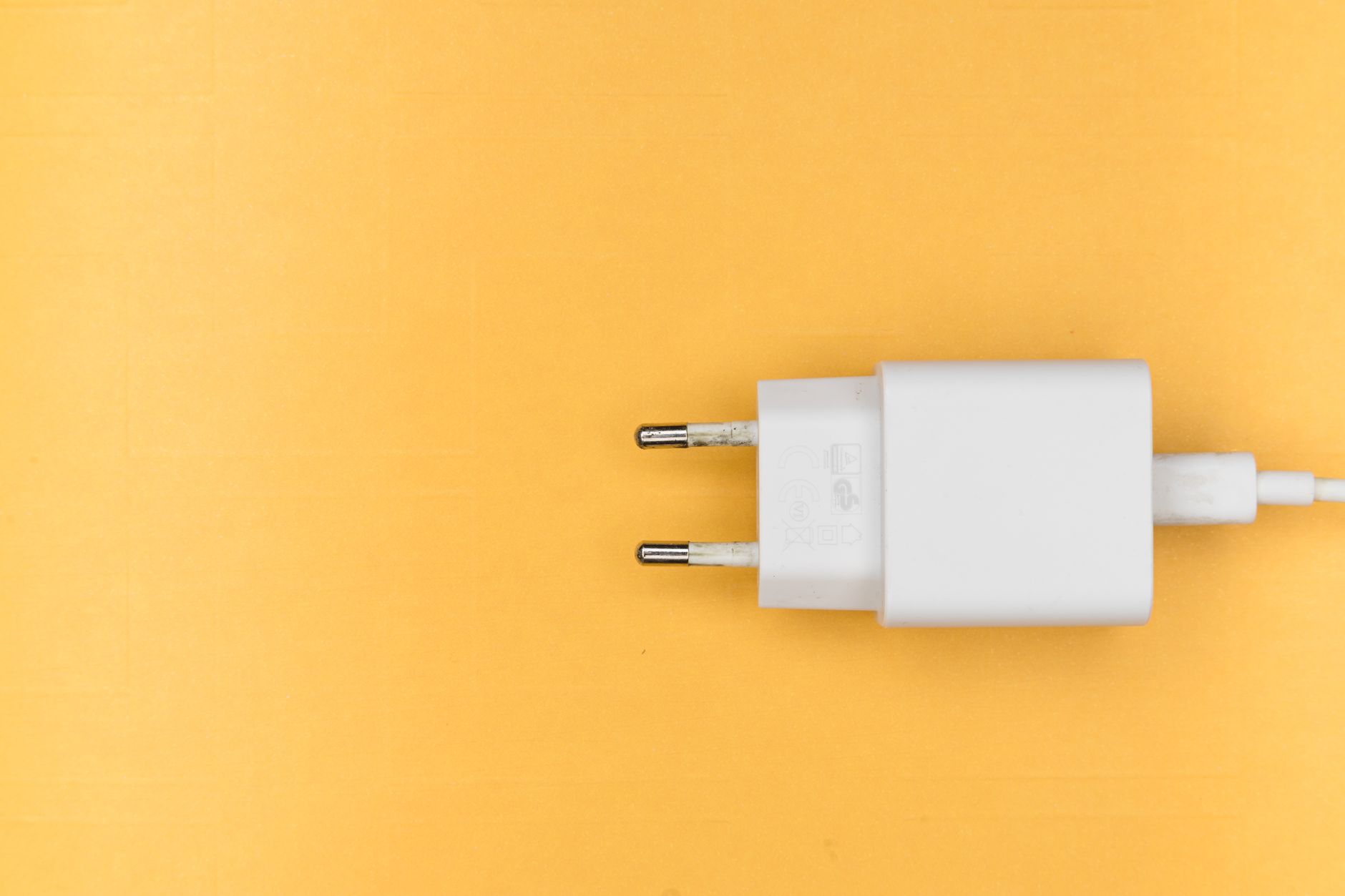 A white phone charger plug on a yellow background