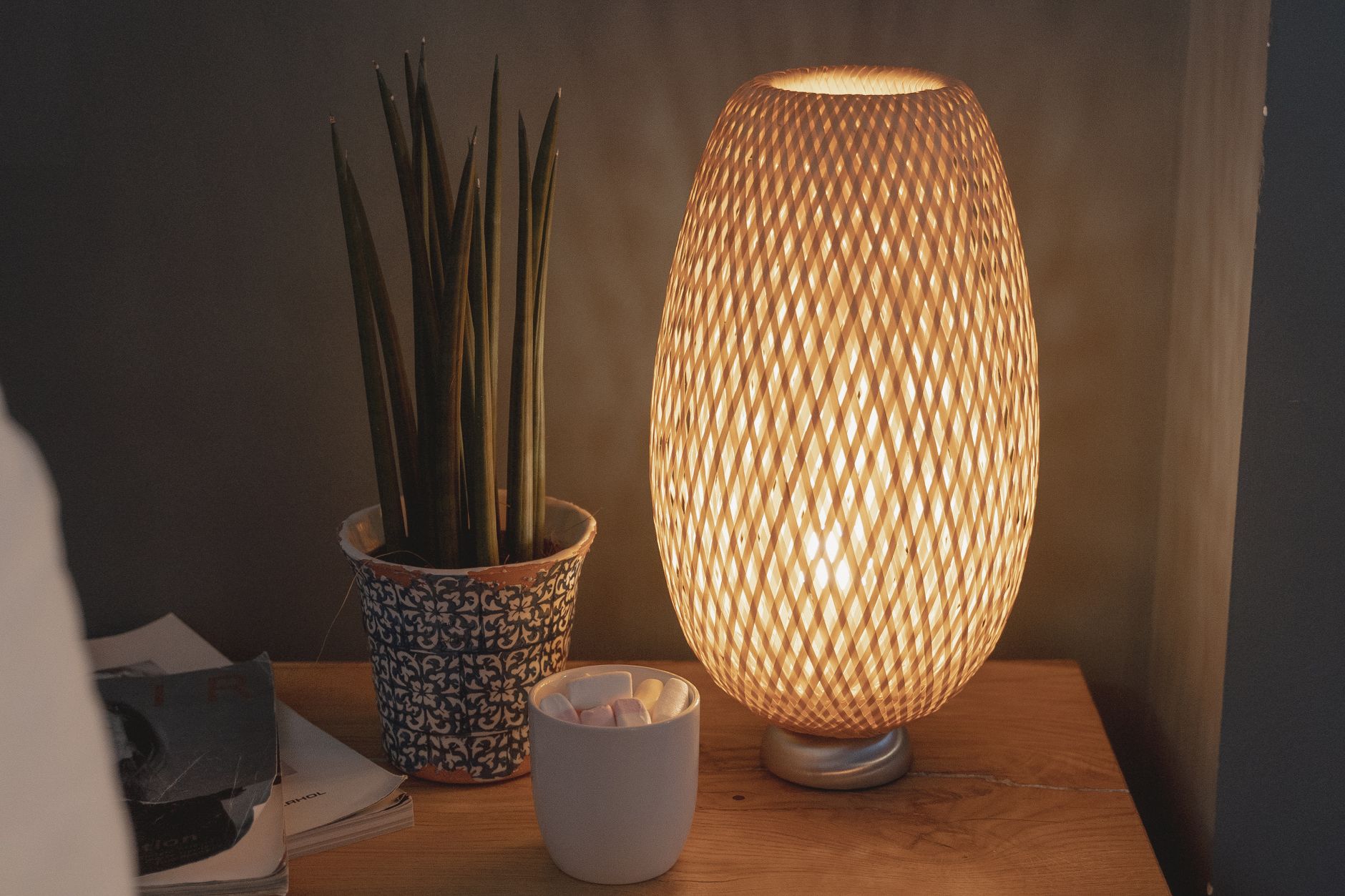 A woven table lamp glowing on a nightstand