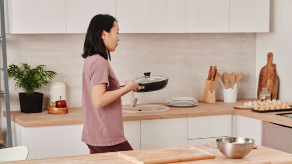 Best pot and pan organizer: a woman carrying a lidded pan in her kitchen