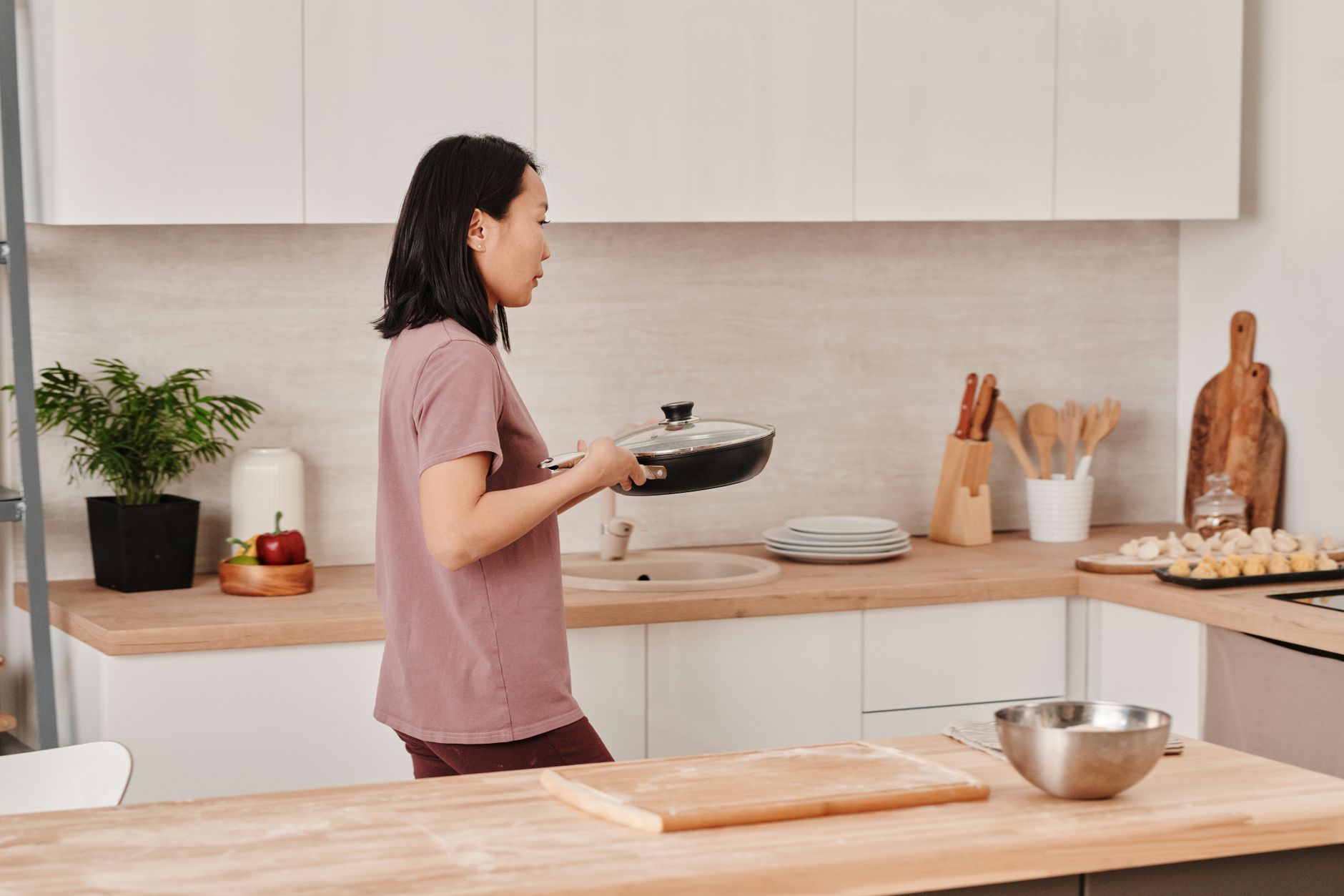 Best pot and pan organizer: a woman carrying a lidded pan in her kitchen
