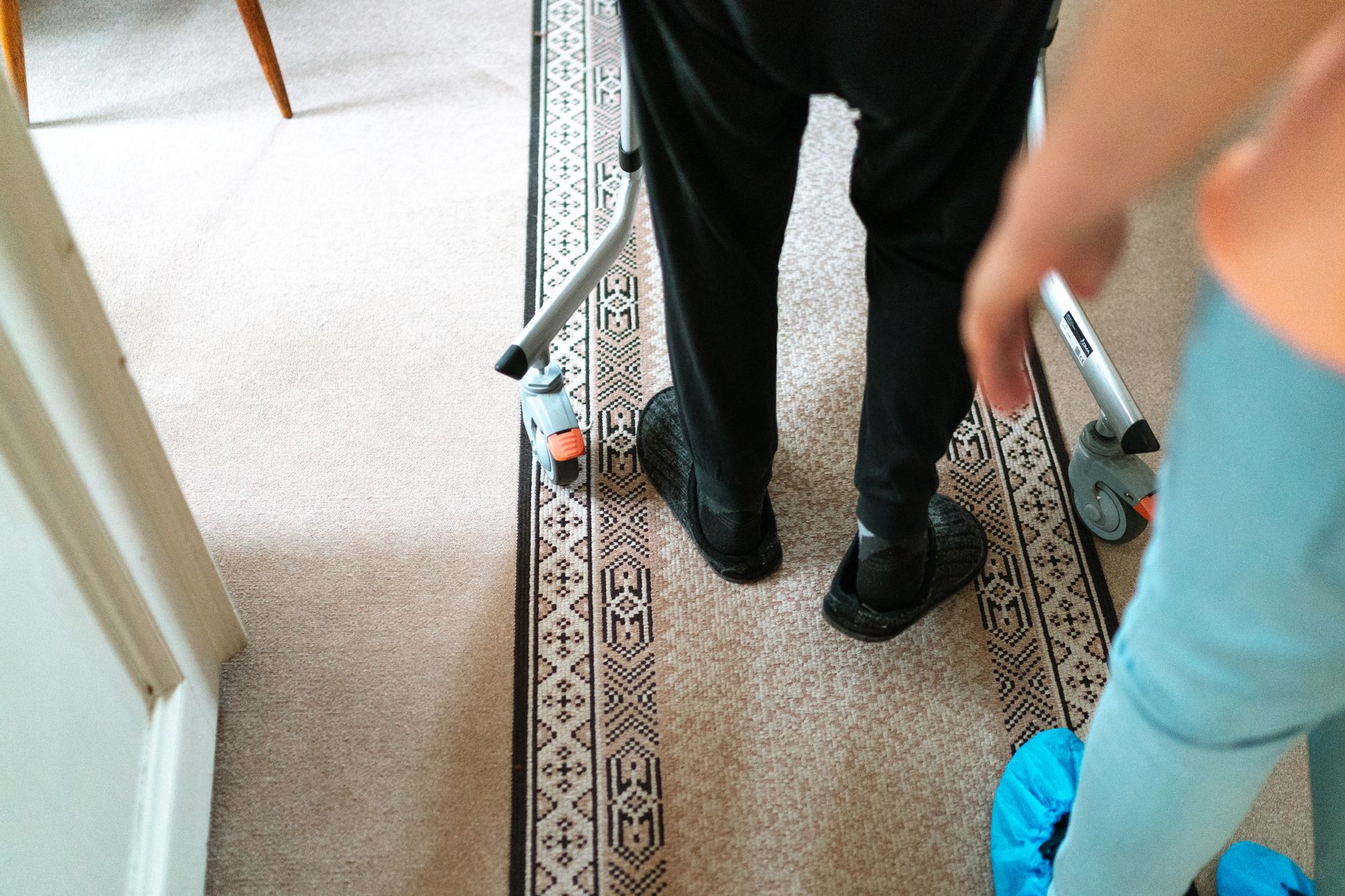 An older person walking with a walker beside a helper
