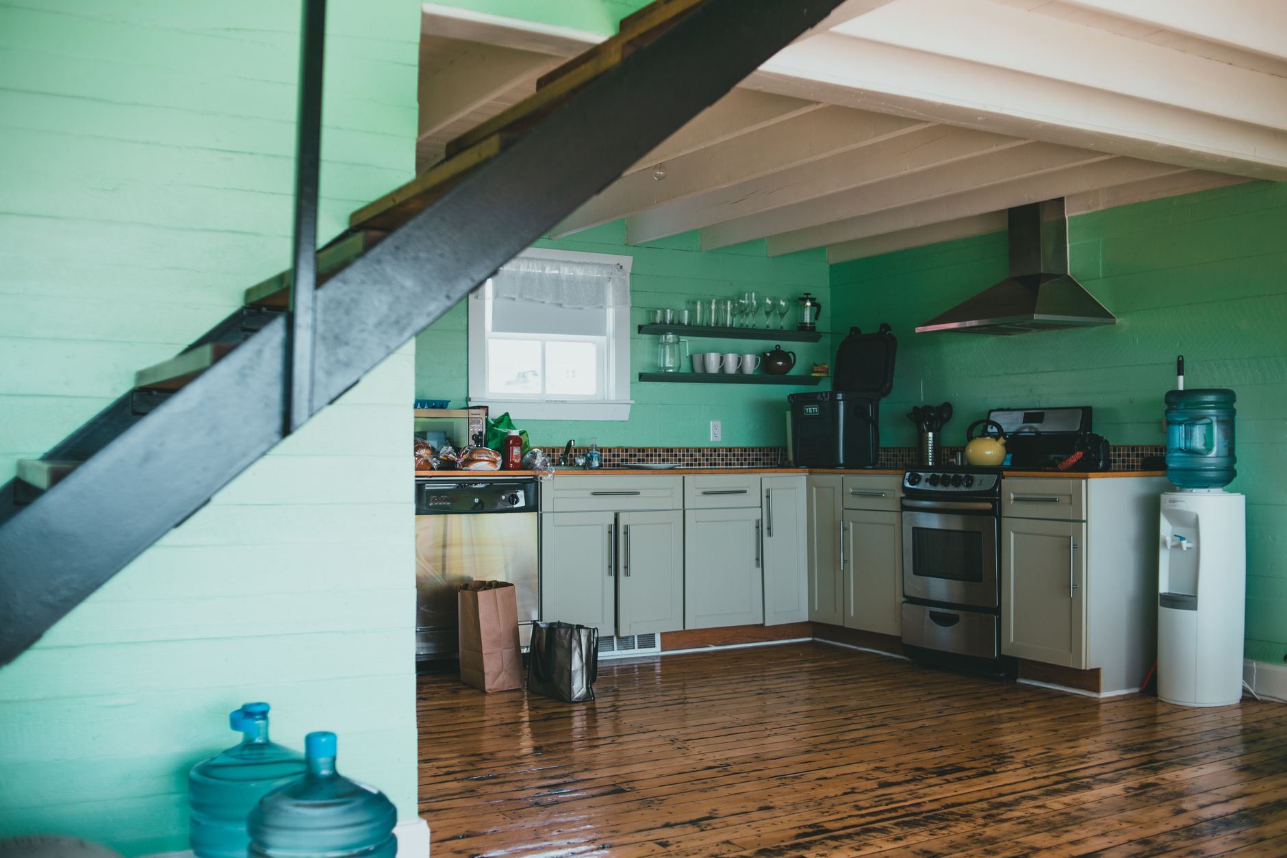 A kitchen under a staircase with water jugs