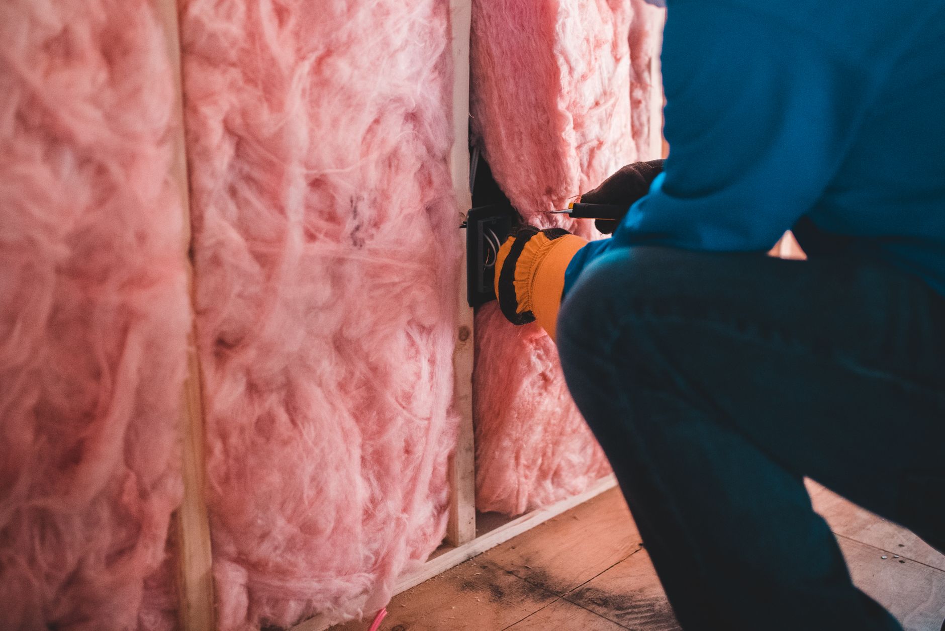 A worker fitting pink insulation between wall studs