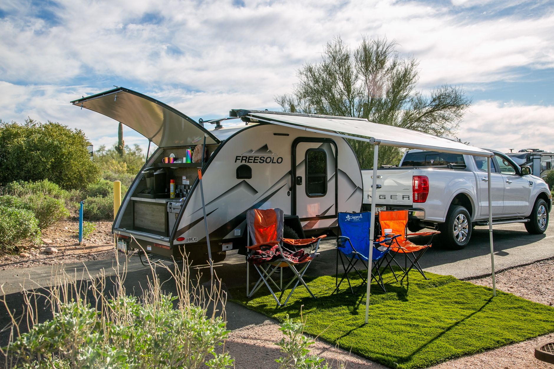 A travel trailer with an awning and chairs