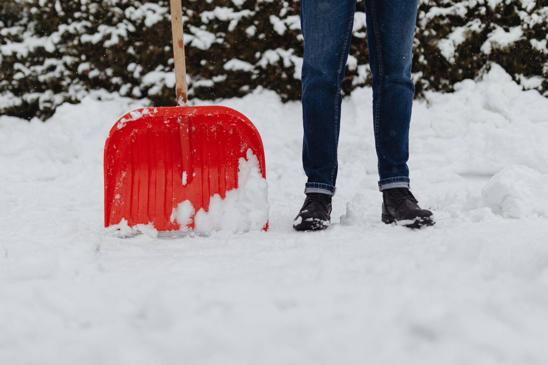A person standing in snow beside a red snow shovel