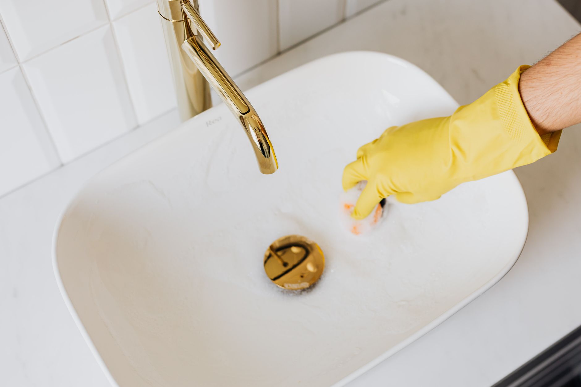 A gloved hand cleaning a bathroom sink