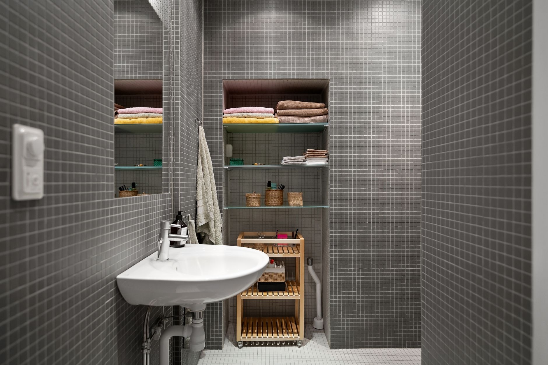 A gray tiled bathroom with shelves of towels