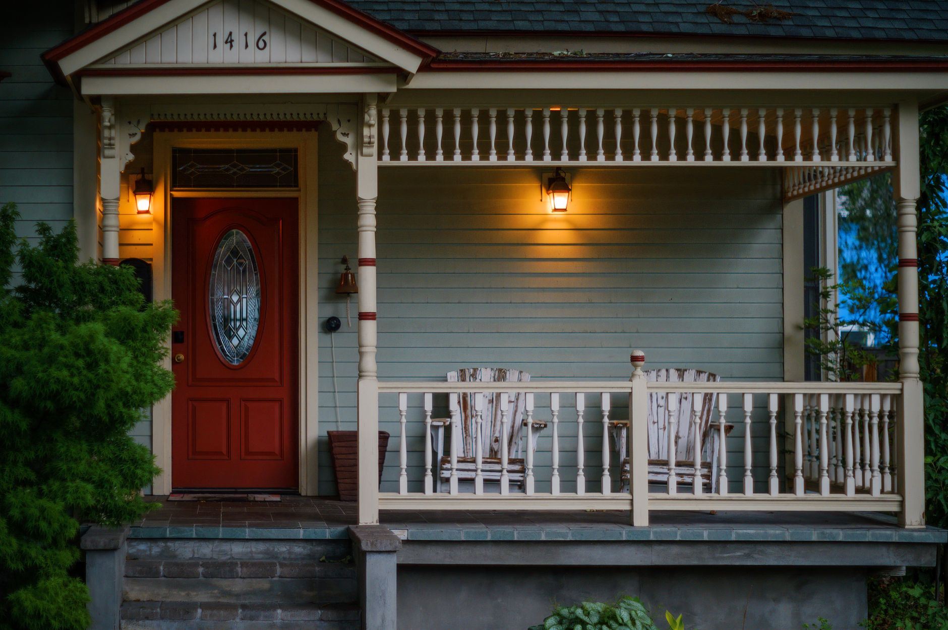 A house porch with a red front door and lamps on at dusk