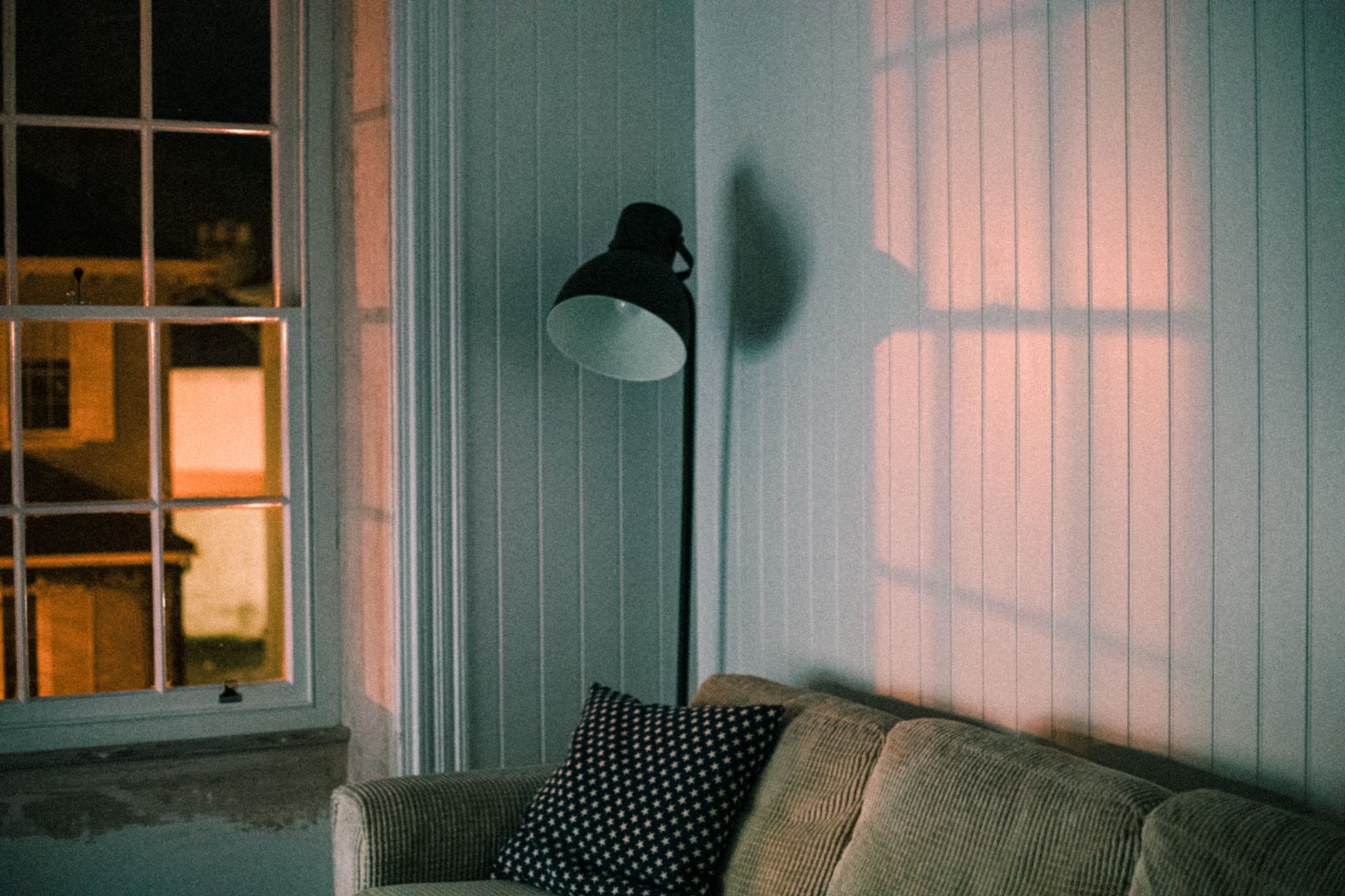 A floor lamp and sofa by a window at dusk