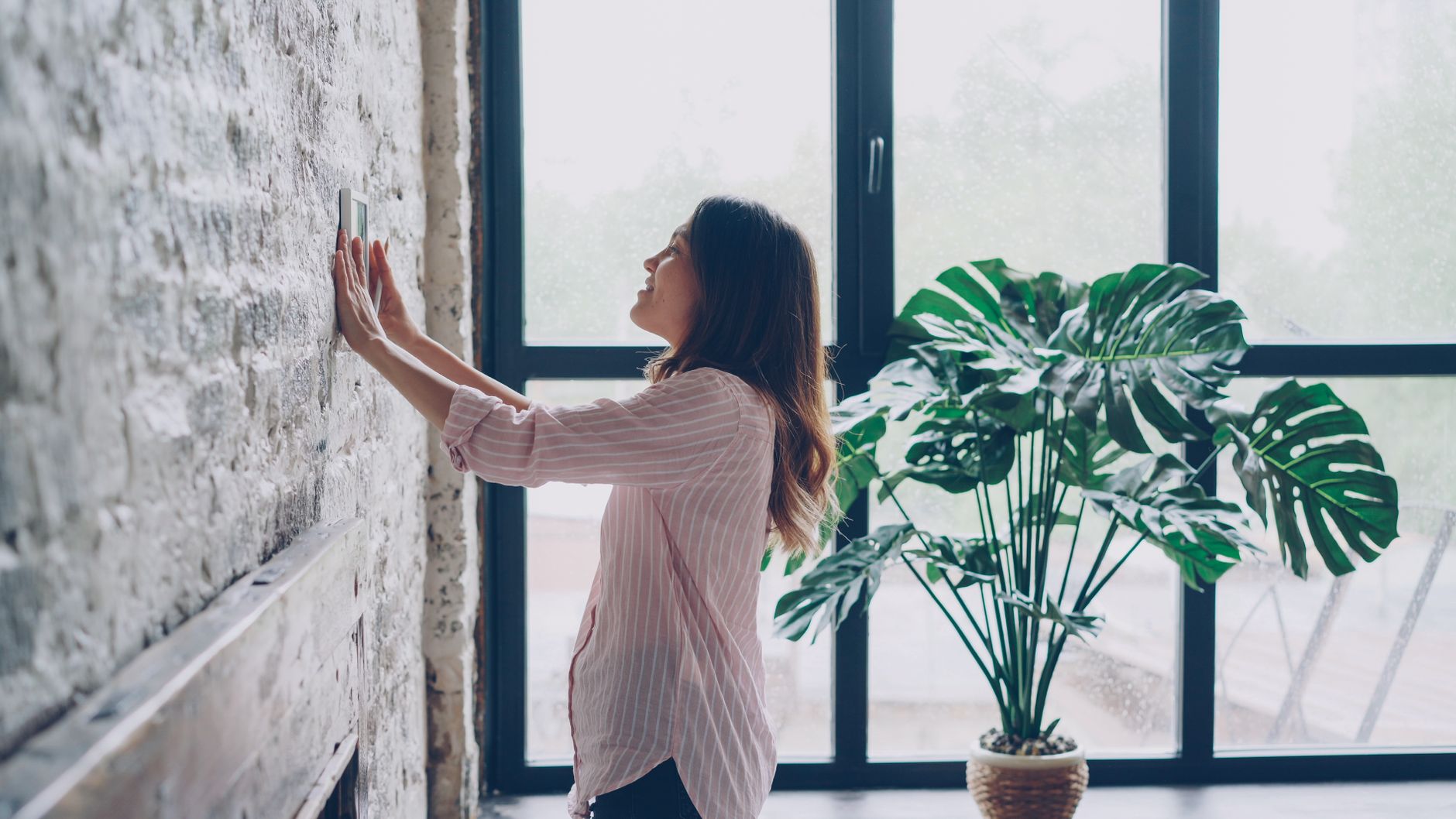 A woman checking a wall by a large window