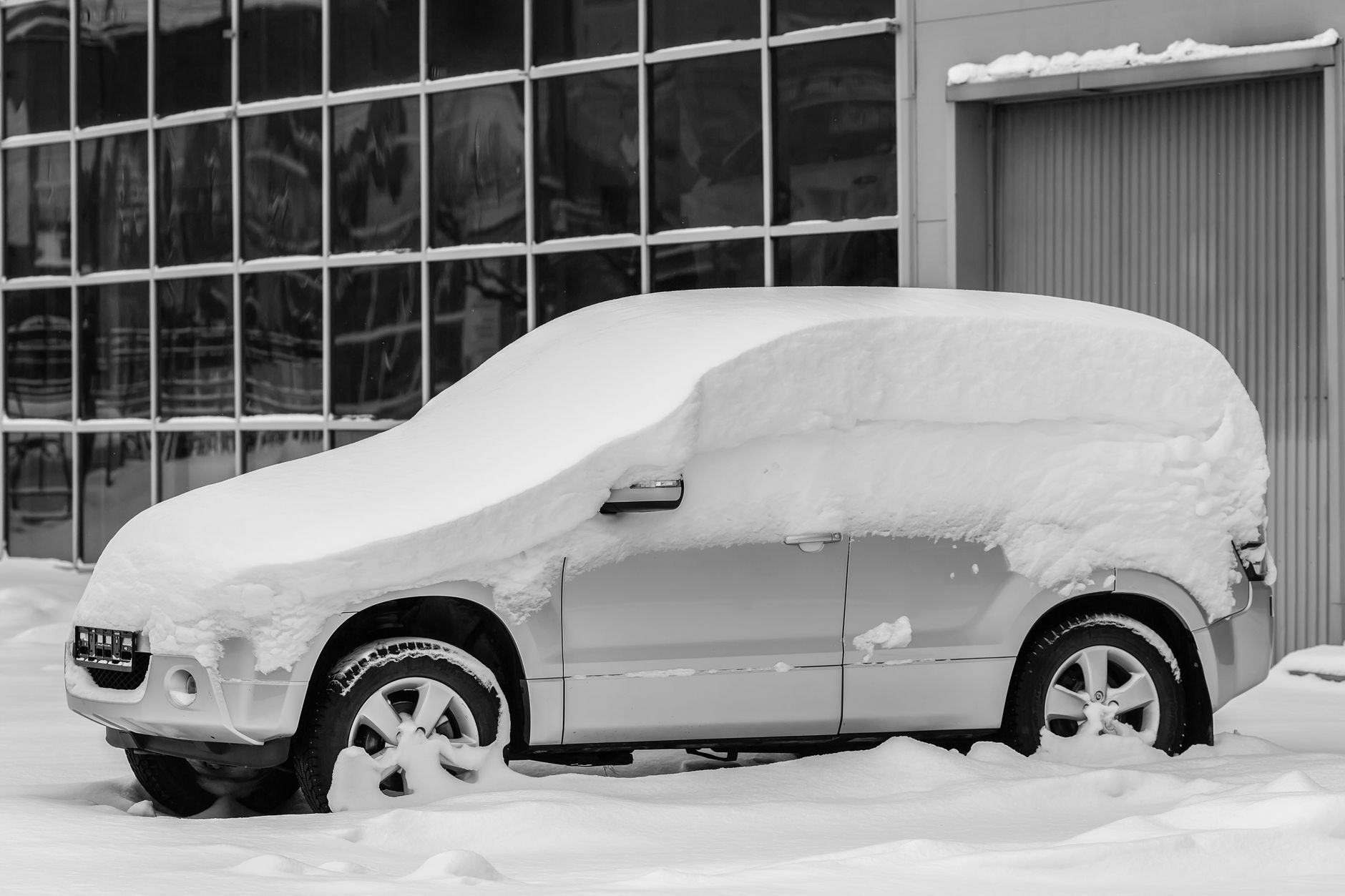 An SUV buried in snow by a building