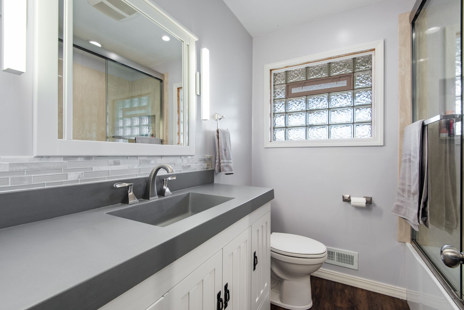 A bathroom with a gray vanity and glass block window