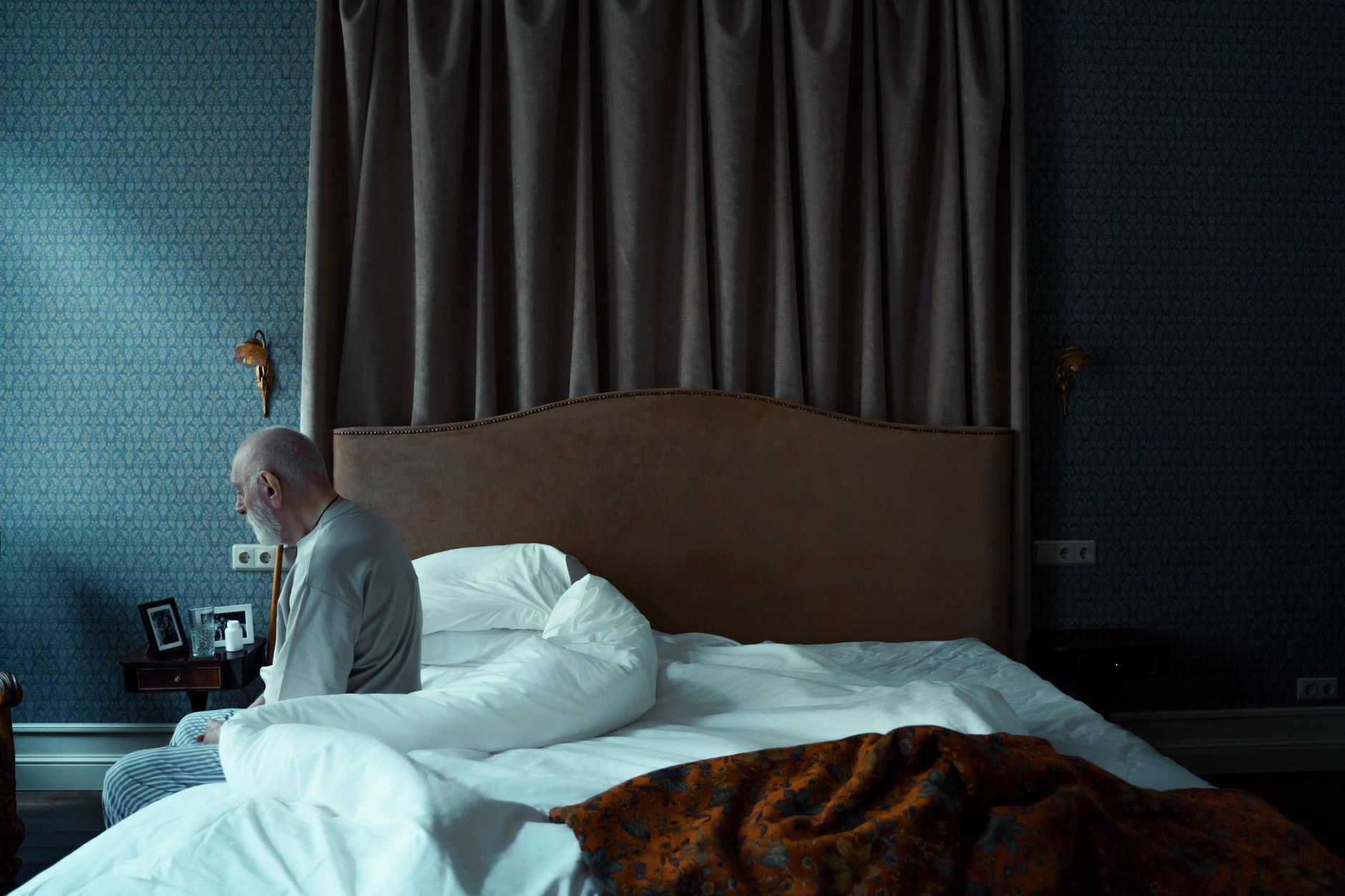 An older man sitting on the edge of a bed