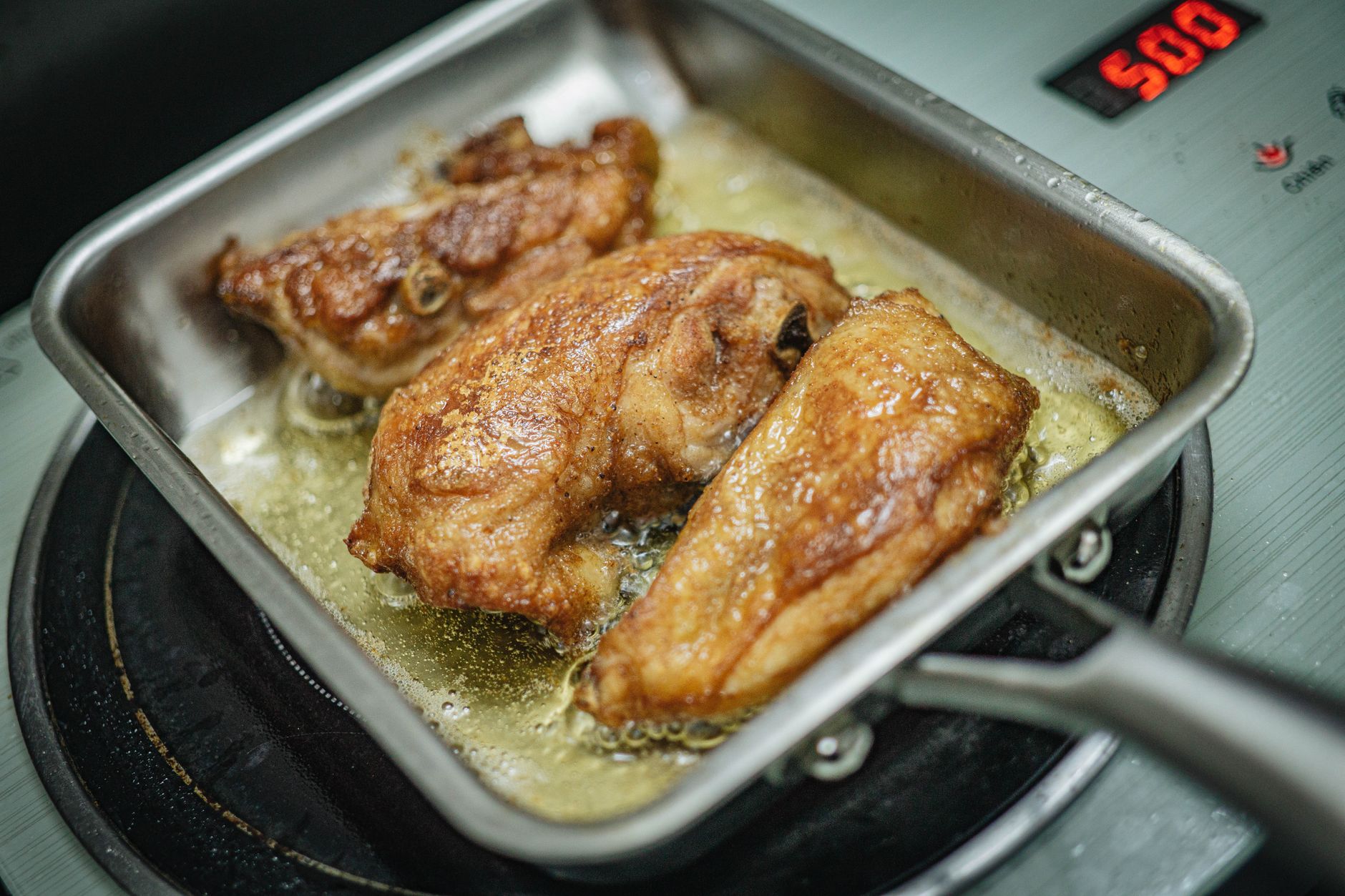 Chicken pieces frying in a square pan