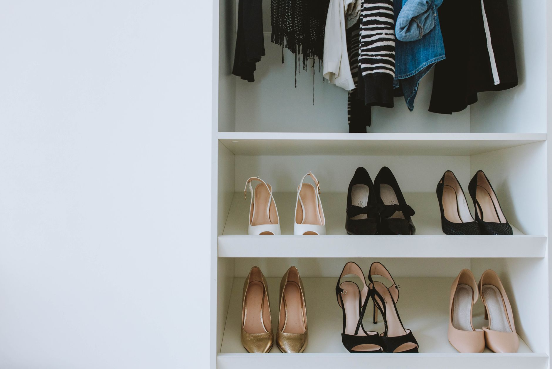 Shoes on shelves below hanging clothes in a closet