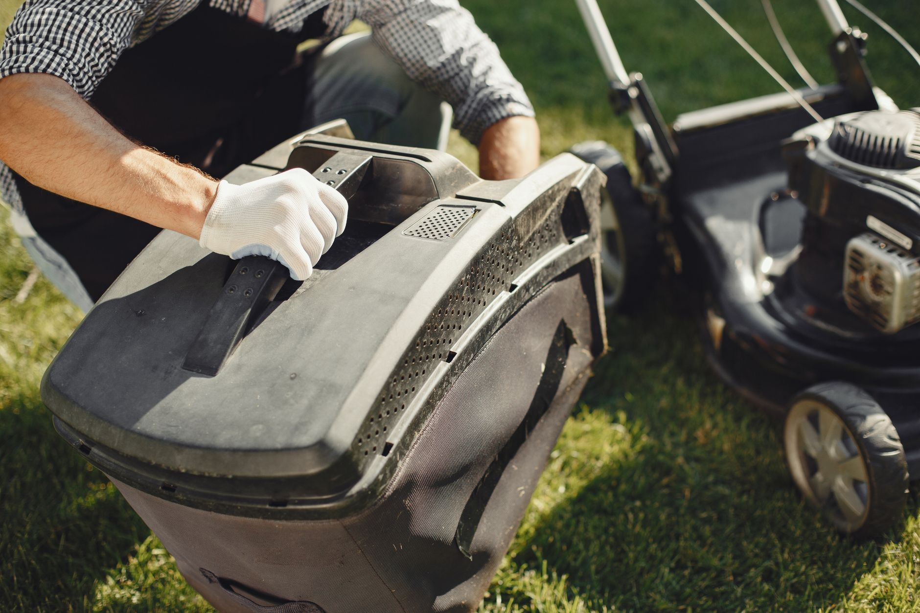 A gloved hand handling a lawn mower bag