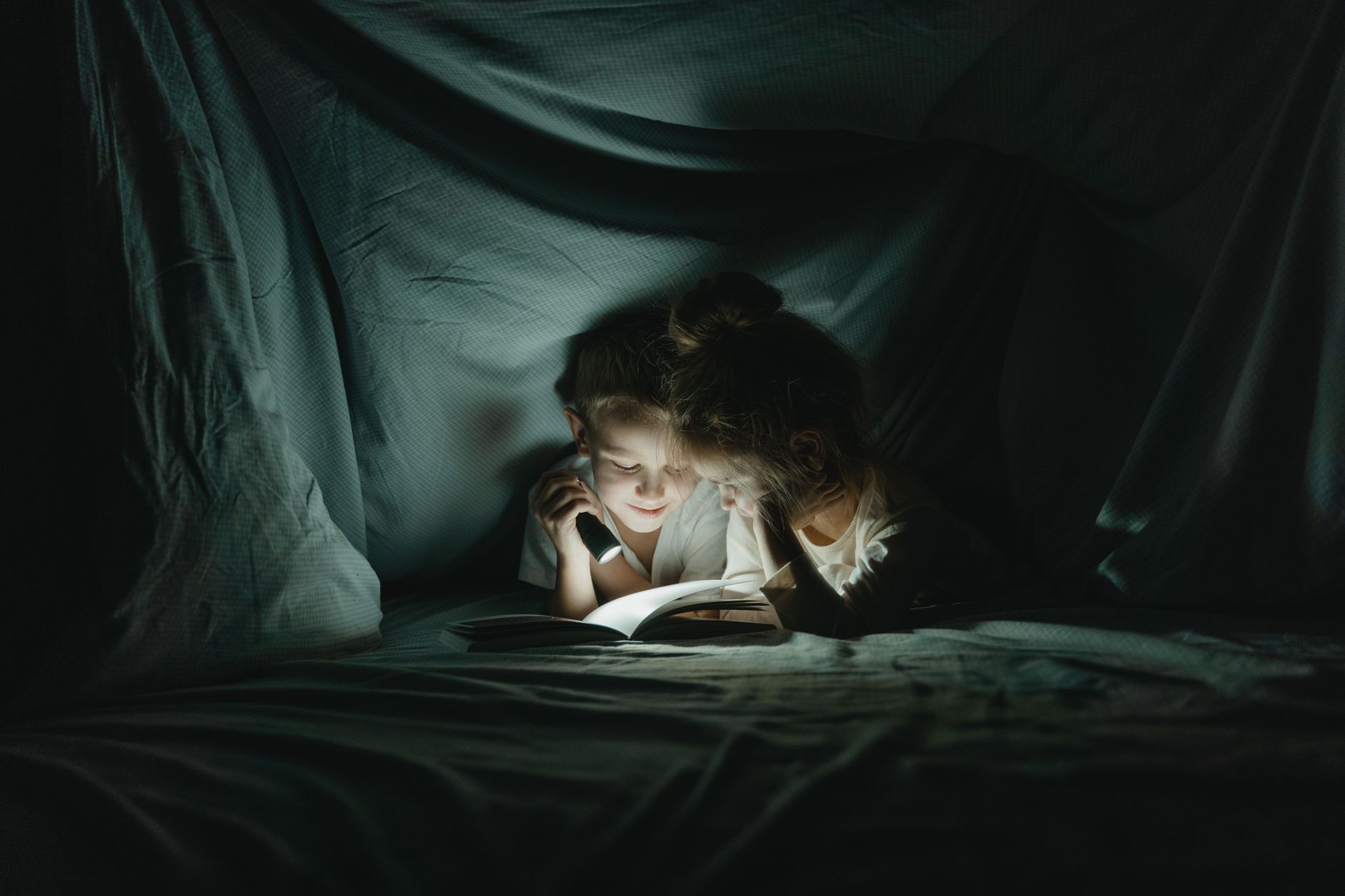 A person reading under a blanket