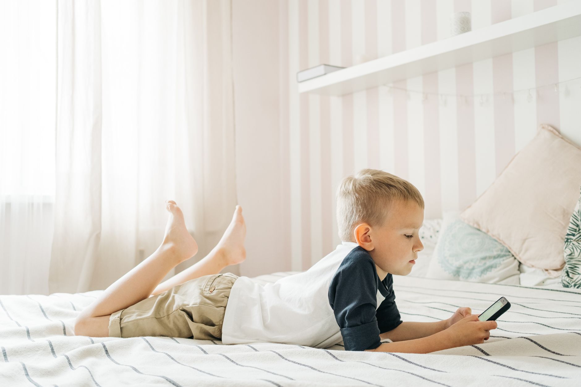 A young boy lying on a bed with a tablet