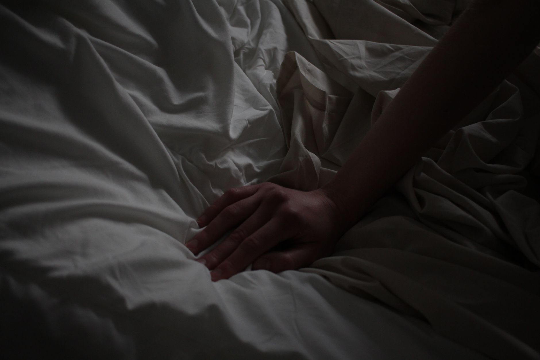 A hand resting on rumpled sheets in a dark room