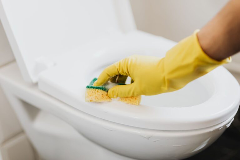 A gloved hand cleaning a toilet seat
