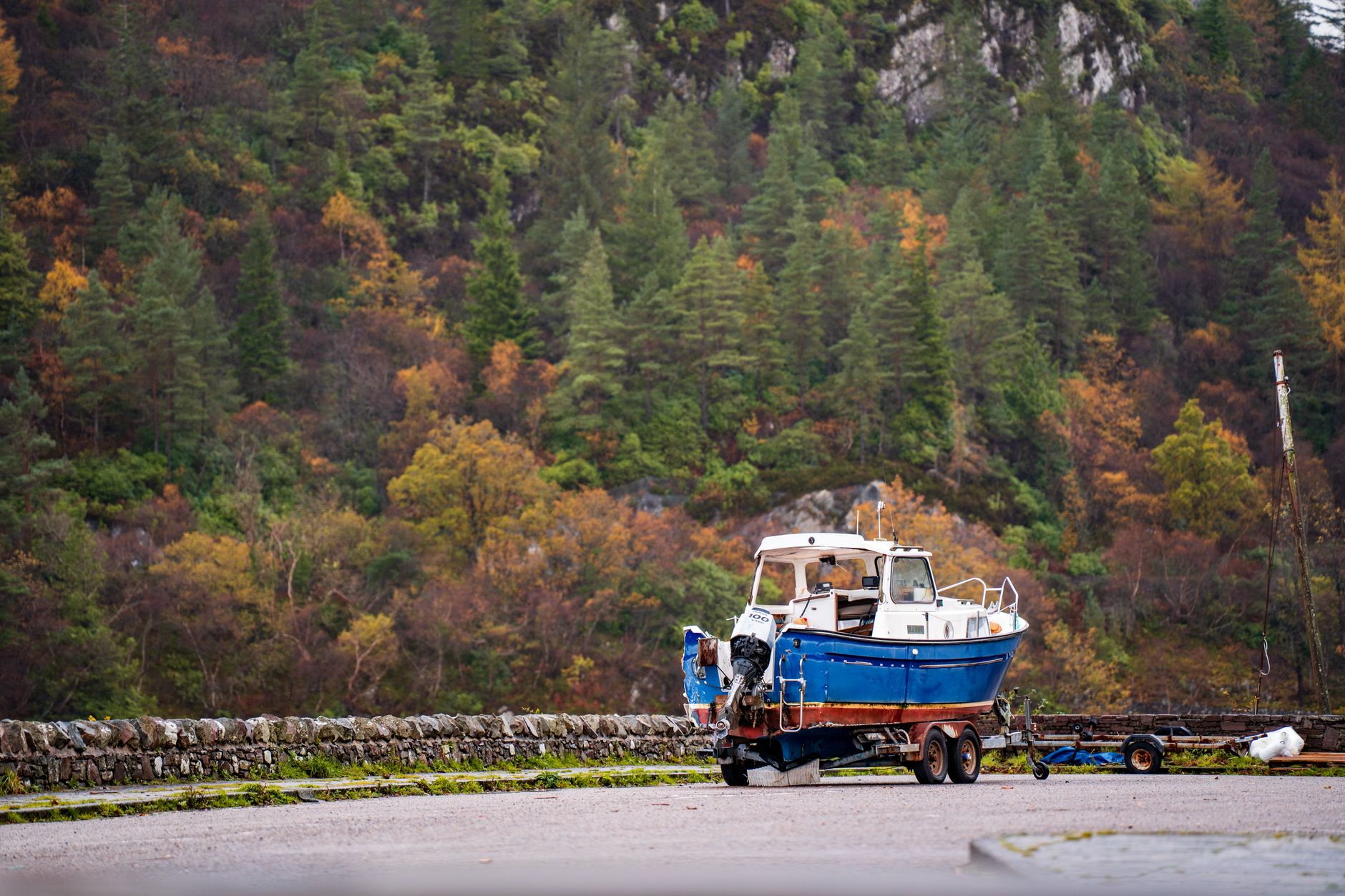 A boat on a trailer by a wooded hillside