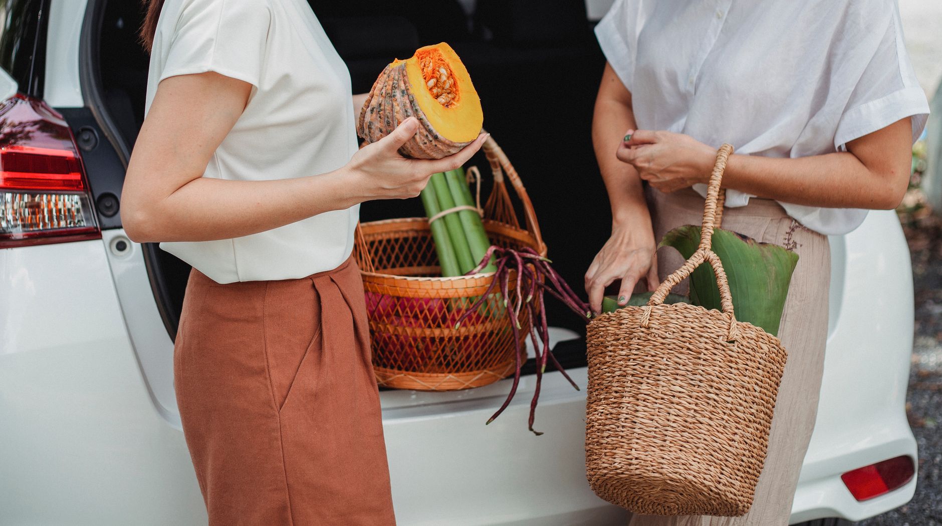 Best trunk organizer: two women putting baskets of produce in a car trunk