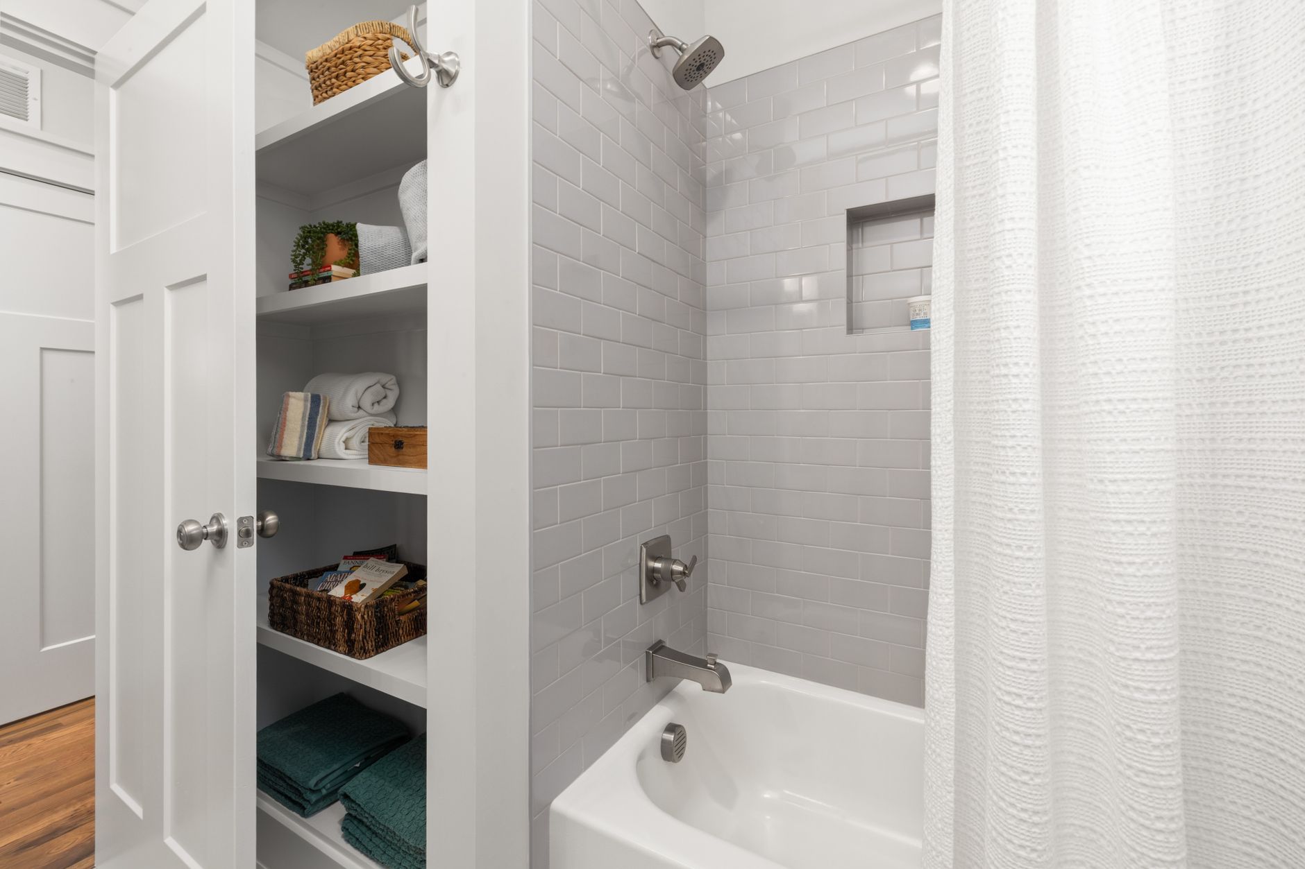 A linen closet next to a tub and shower