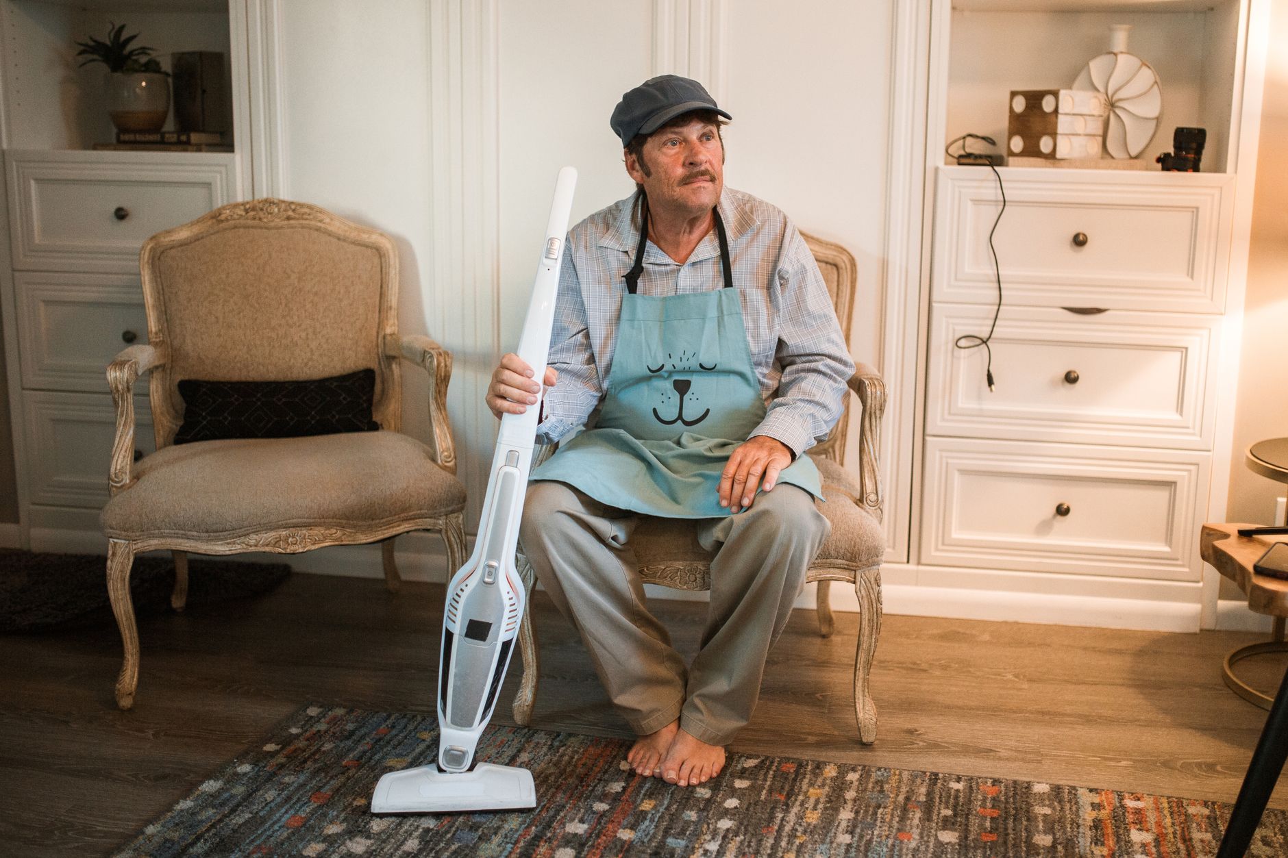 Man sitting with a cordless stick vacuum on a rug