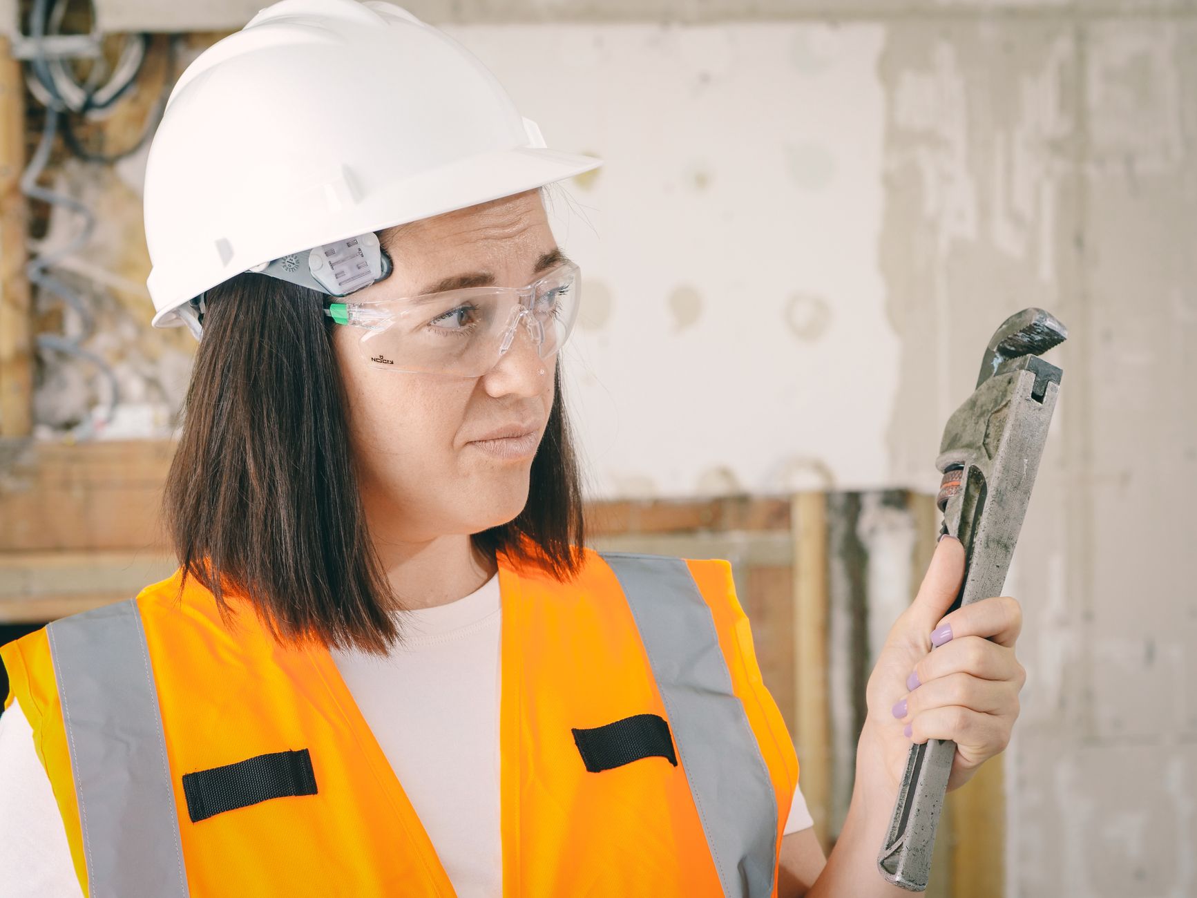 A woman in a hard hat holding a pipe wrench