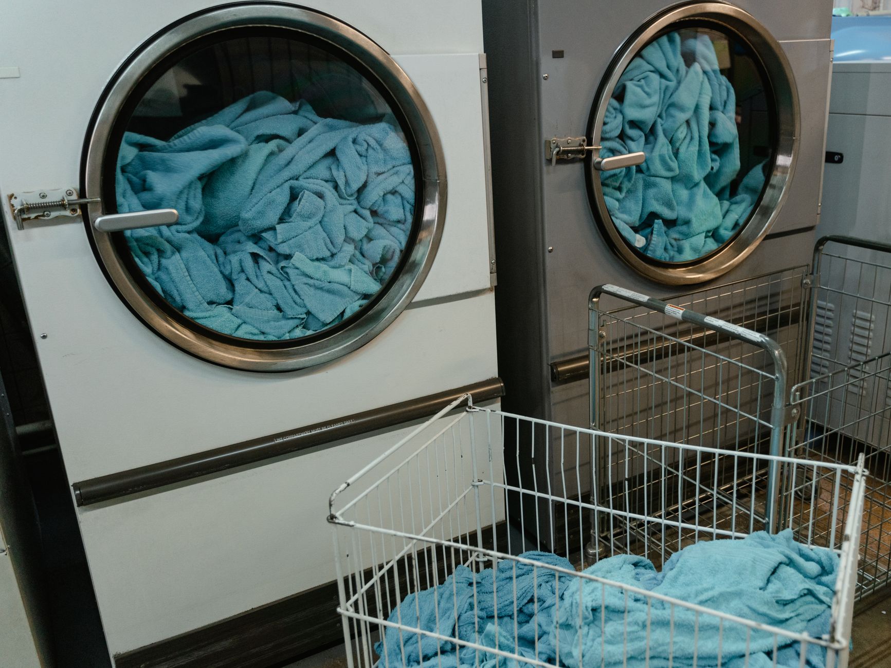 Front-loading washers full of towels beside a laundry cart
