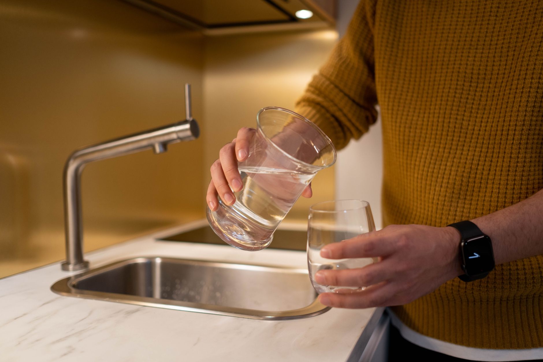 Person holding glasses of water at a kitchen sink